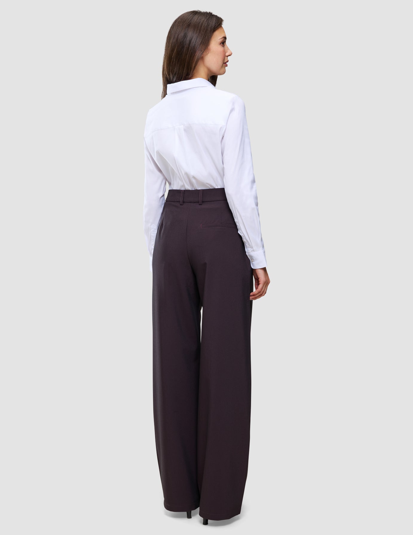 Eine Frau, von hinten gesehen, die ein weißes Hemd trägt, das in die Damenhose Avira Pants Wide in der Farbe Burgundy Berry gesteckt ist.